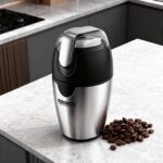 Molinillo de cafe de acero inoxidable en una encimera de cocina junto con granos de café