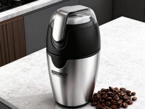 Molinillo de cafe de acero inoxidable en una encimera de cocina junto con granos de café